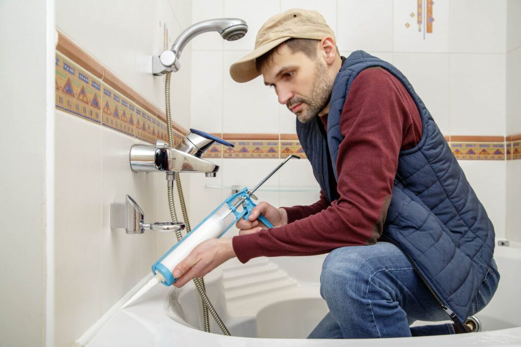 60224691 - Plumber Caulking Bathtub With Silicone Glue Using Caulking Gun.